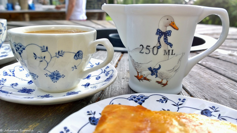 Kahvikuppi, pieni maitokannu ja piirakkapala