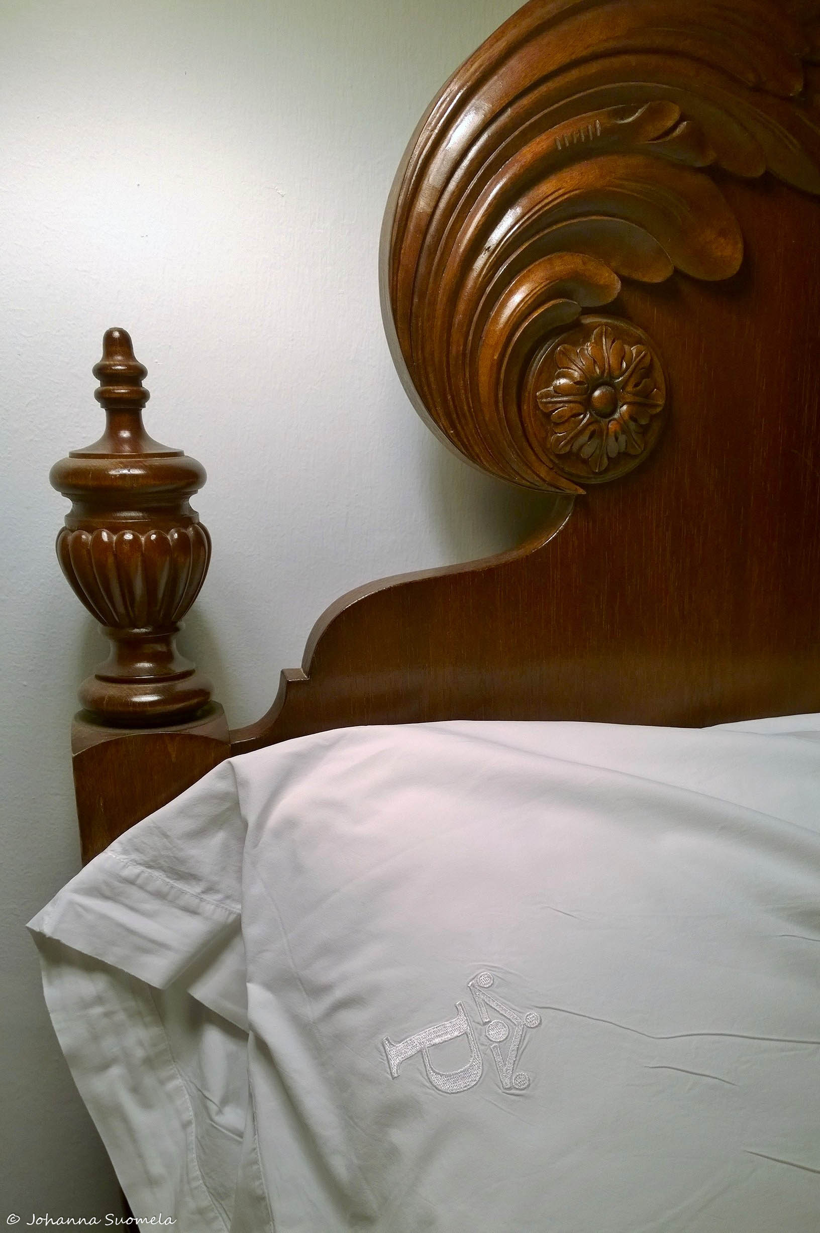 Kaunis ruskeasta puusta veistetty sängynpääty ja laadukas applikoitu lakana La Gomeran Parador-hotellissa